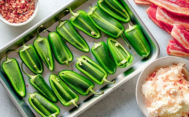 Подготовка халапеньо для фарширования Разрезанные вдоль перцы халапеньо на противне с пергаментом
